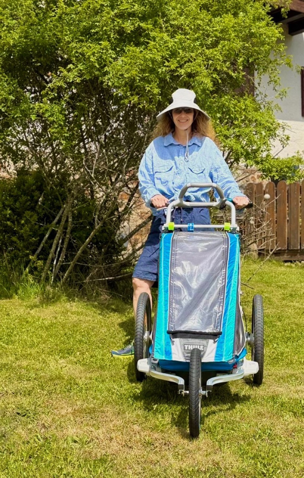 A blue three-wheeled pram on grass in Germany